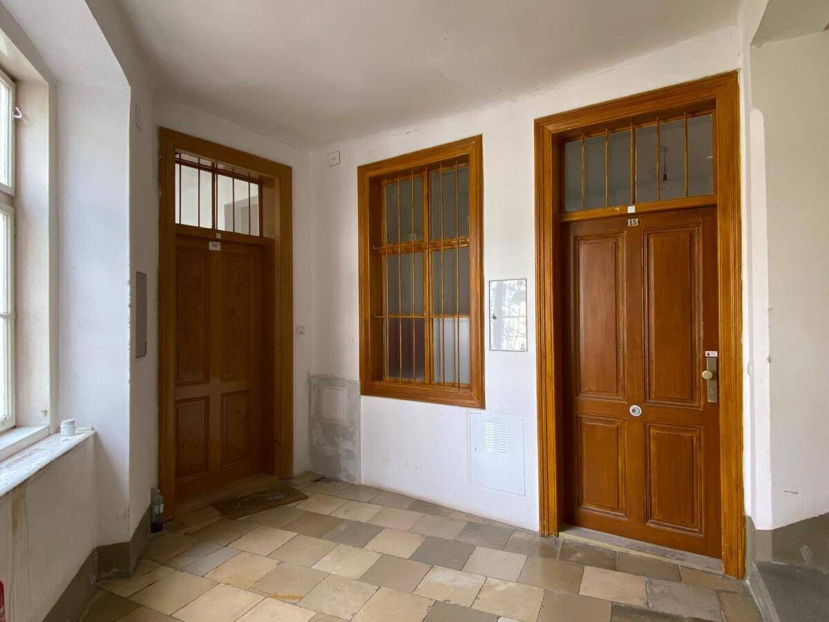 Heller Hausflur mit zwei Holztüren und einem Fenster mit Gitter, gefliester Boden.