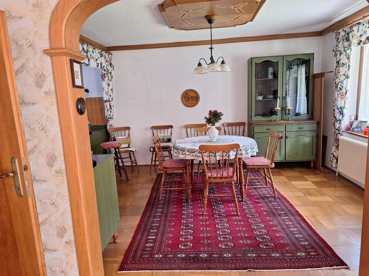Gemütliches Esszimmer mit traditionellen Holzmöbeln, Teppich und einem grünen Buffet, strahlt Wärme aus.