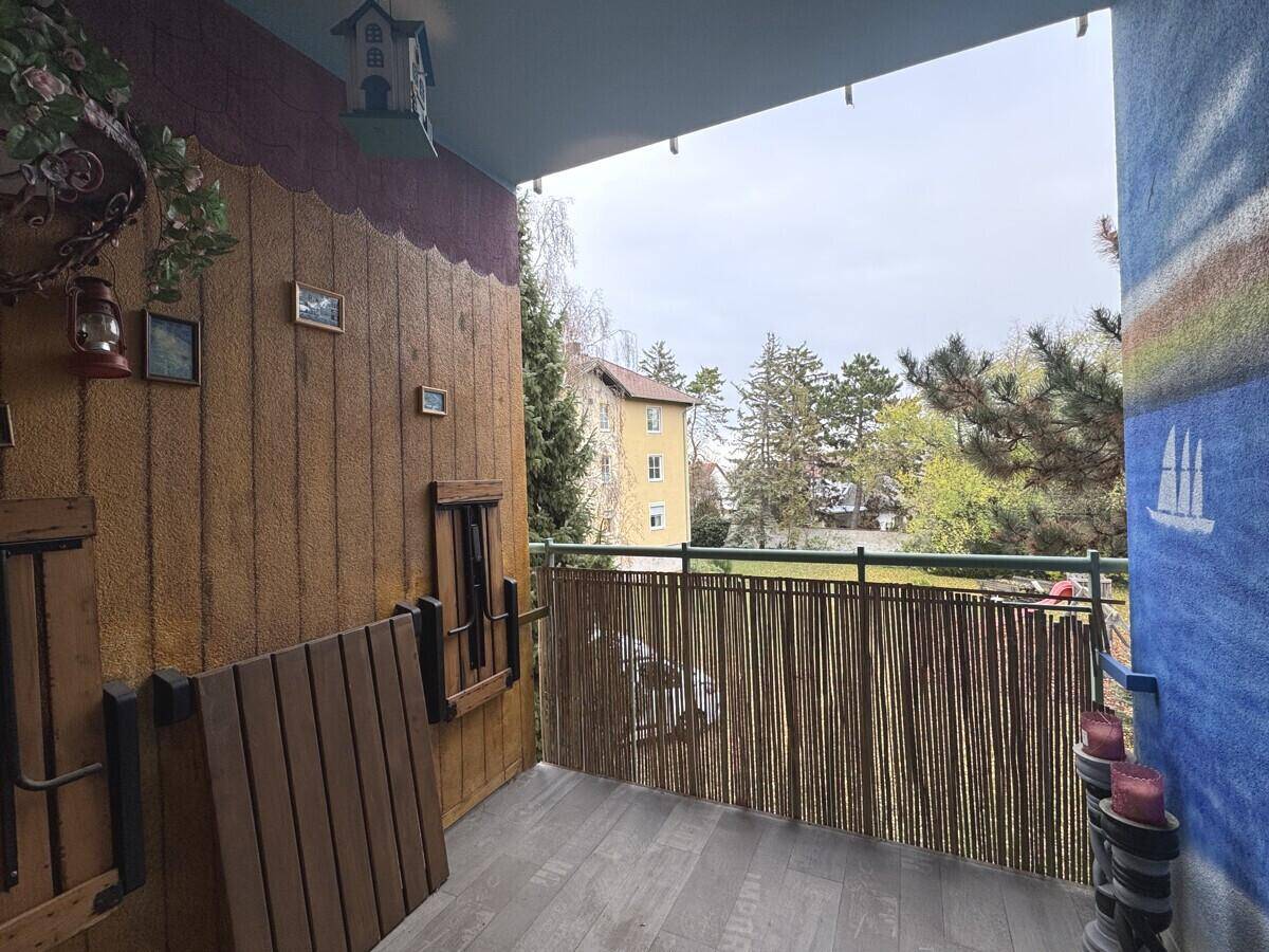 Dekorierter Balkon mit Holzboden, Sichtschutz und Blick ins Grüne.
