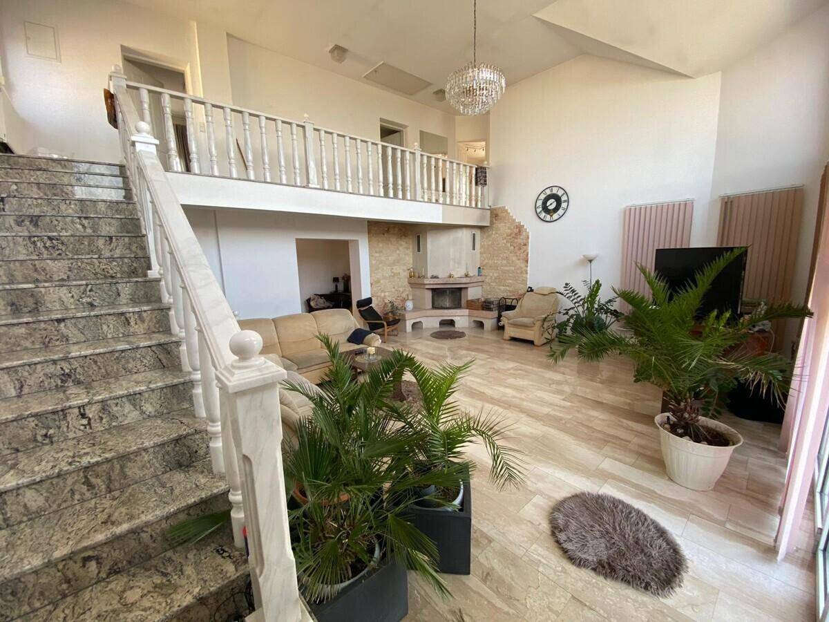 Geräumiges Wohnzimmer mit hohen Decken, elegantem Kamin und einer Marmortreppe, die zu einer Galerie führt.
