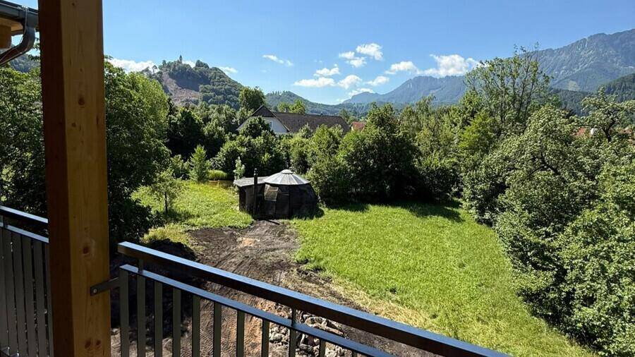 Balkon mit weitem Blick über grüne Wiesen, ein kleines Gartenhaus und die beeindruckende Bergkulisse.