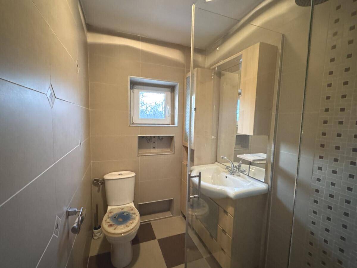 Gefliestes Badezimmer mit Dusche, WC, Waschbecken und einem kleinen Fenster für Tageslicht.