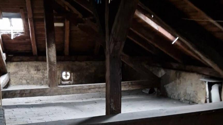 Unausgebauter Dachboden mit sichtbaren Holzbalken und kleinem Fenster, bietet Ausbaupotenzial.