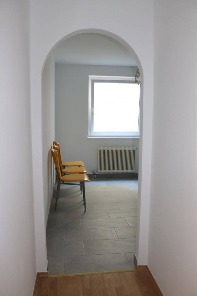 Blick durch einen Bogen in einen Raum mit Fliesenboden, Fenster und Heizkörper.