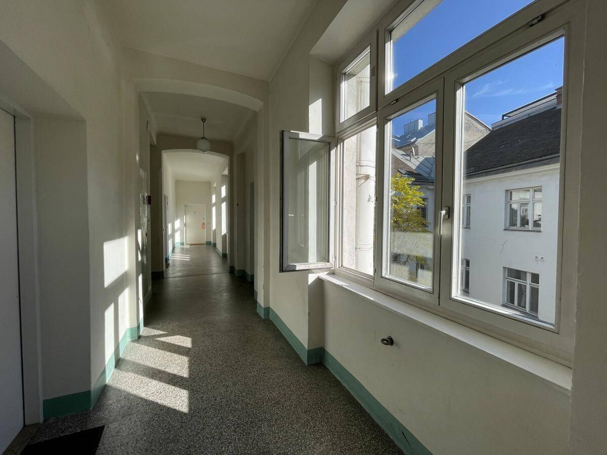 Heller Flur eines Altbaus mit großen Fenstern und Blick in den sonnigen Innenhof.