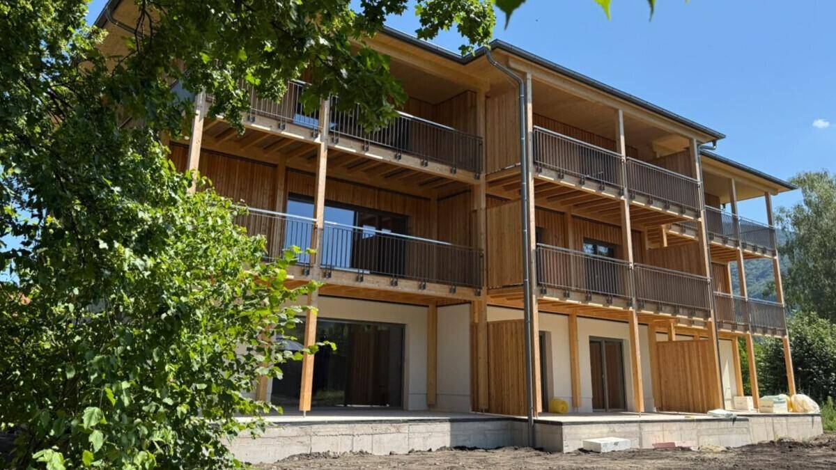 Modernes Holzgebäude mit mehreren Balkonen und großen Fensterfronten, umgeben von üppiger Natur.