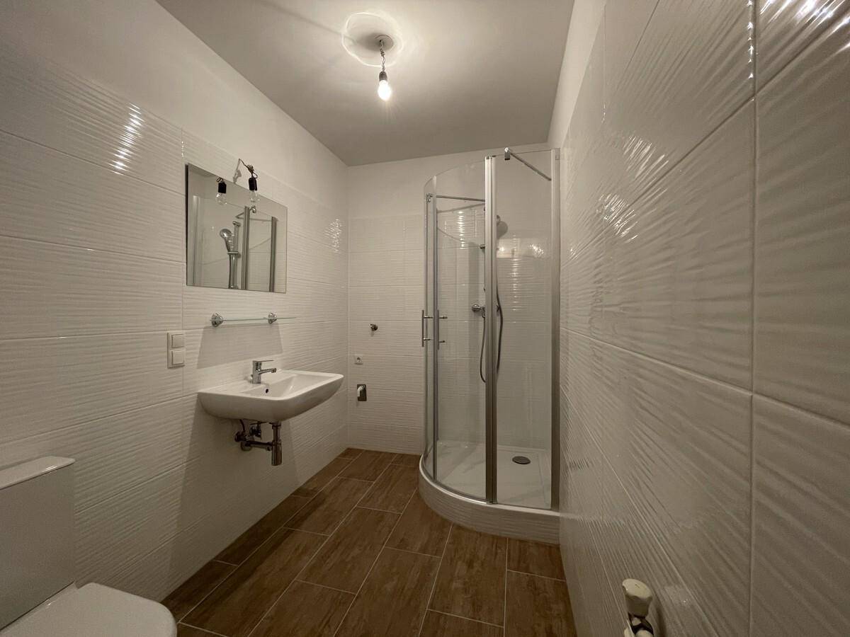 Modernes Badezimmer mit weißen strukturierten Fliesen, Holzoptik-Bodenfliesen und einer Duschkabine.