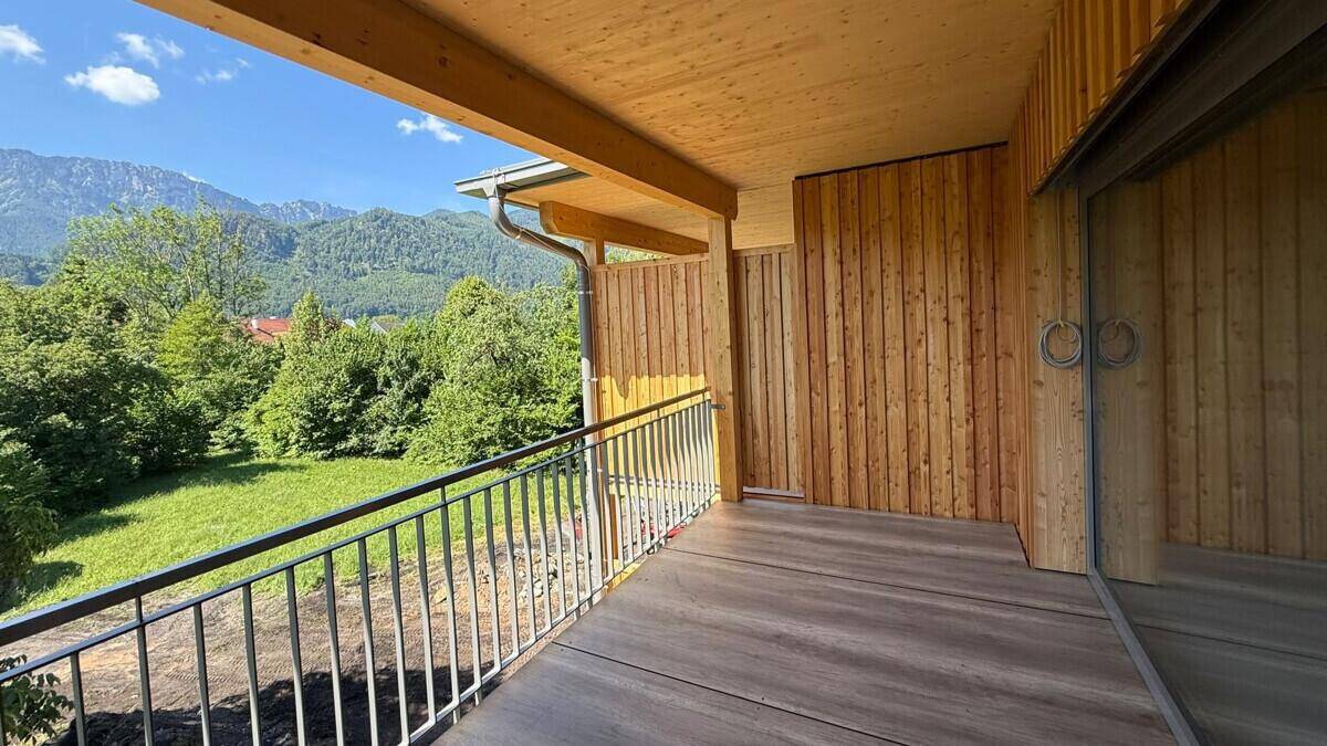 Geräumiger Balkon mit Holzboden und Blick auf die umliegende Berglandschaft und grüne Wiesen.
