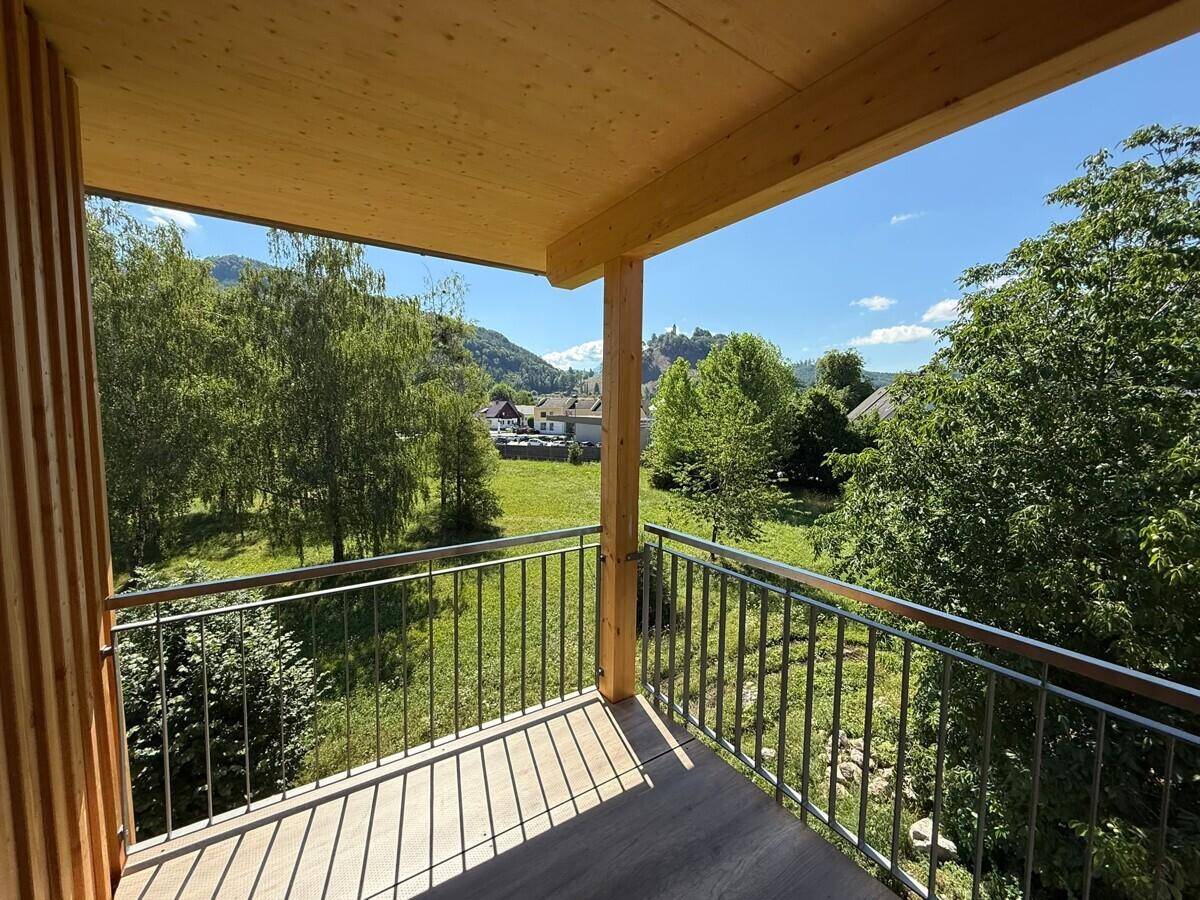 Sonniger Balkon mit Holzboden und Geländer, bietet einen weiten Blick auf die grüne Landschaft und Berge.