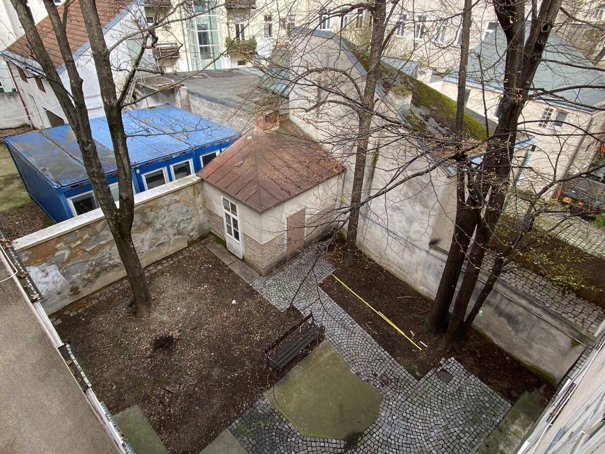 Innenhof mit altem Schuppen, Bäumen und einer Bank, bietet Potenzial zur Gestaltung.