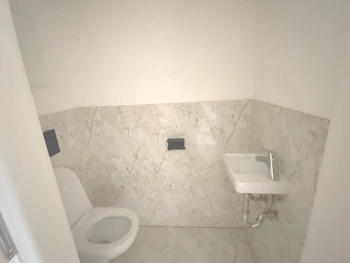 Gäste-WC mit wandmontierter Toilette, kleinem Waschbecken und eleganten Marmorfliesen.