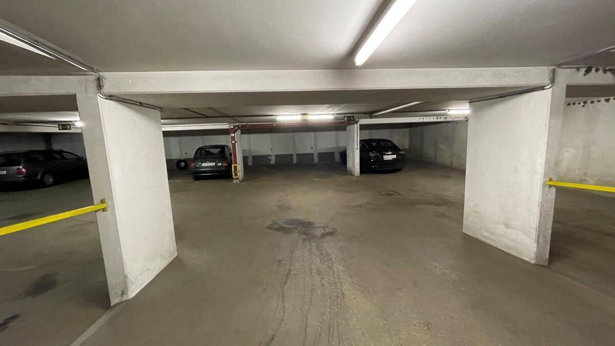 Tiefgarage mit mehreren Stellplätzen und Betonwänden, beleuchtet von Leuchtstoffröhren.