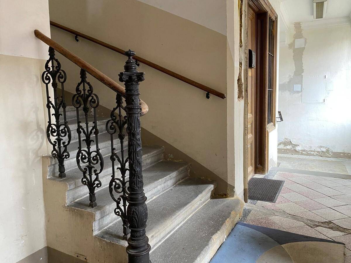 Historisches Treppenhaus mit schmiedeeisernem Geländer, Steinstufen und gemustertem Fliesenboden in einem Altbau.
