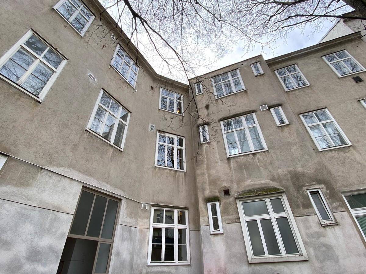 Fassade eines Altbaus im Innenhof mit zahlreichen Fenstern und schlichter Putzfassade.