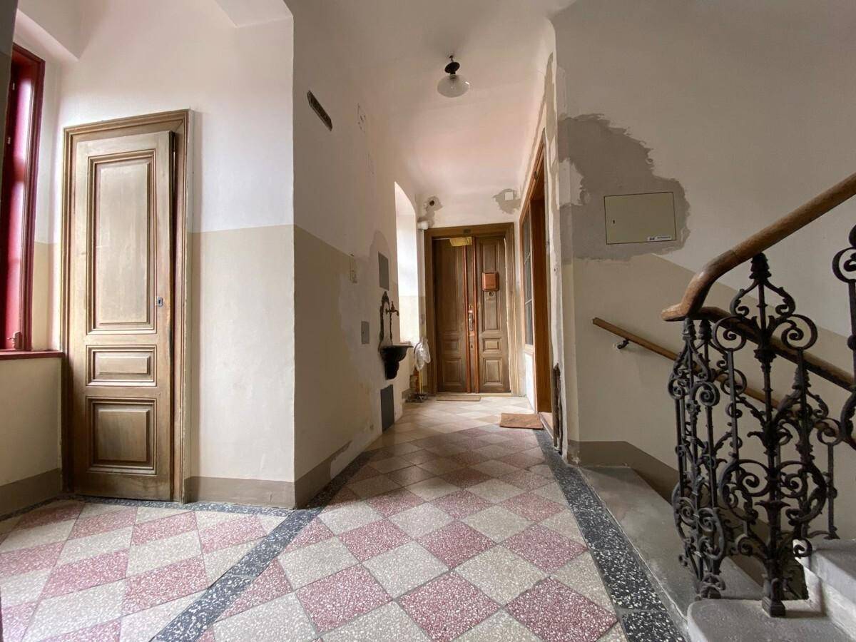 Langer Flur in einem Altbau mit gemustertem Fliesenboden und mehreren Holztüren.