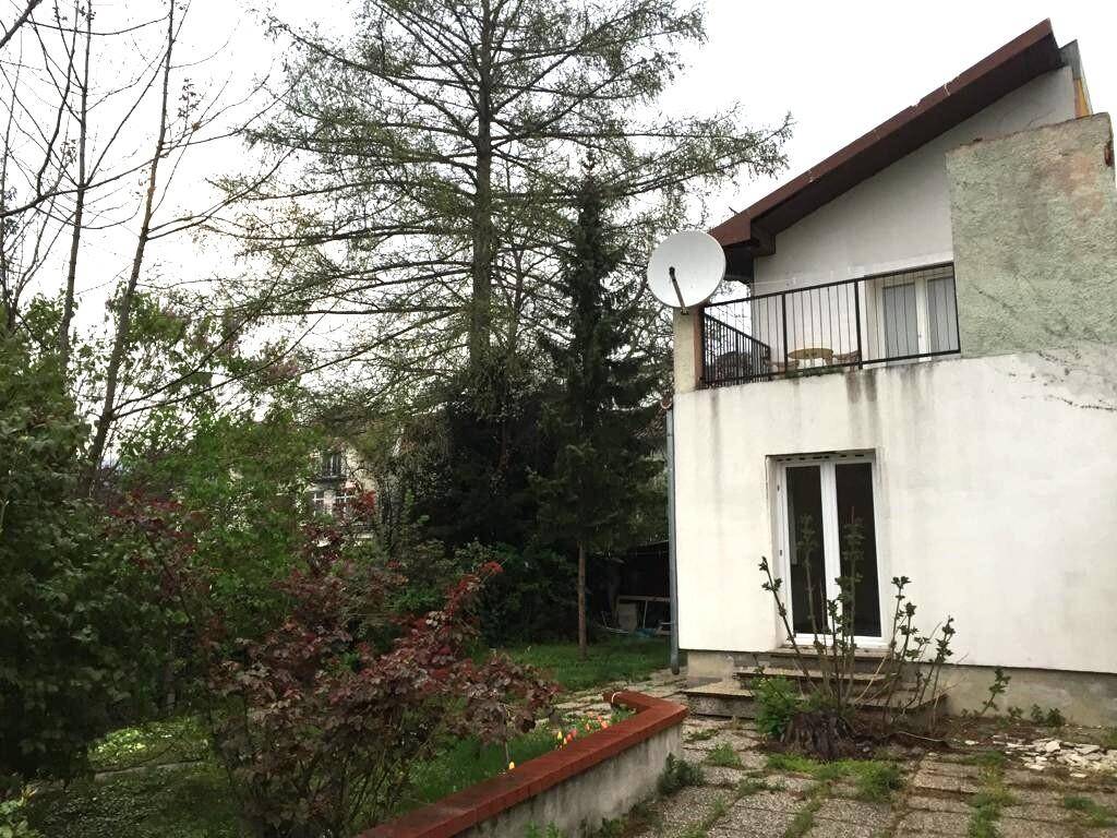 Rückseite eines Hauses mit Balkon, Gartenbereich und altem Baumbestand.