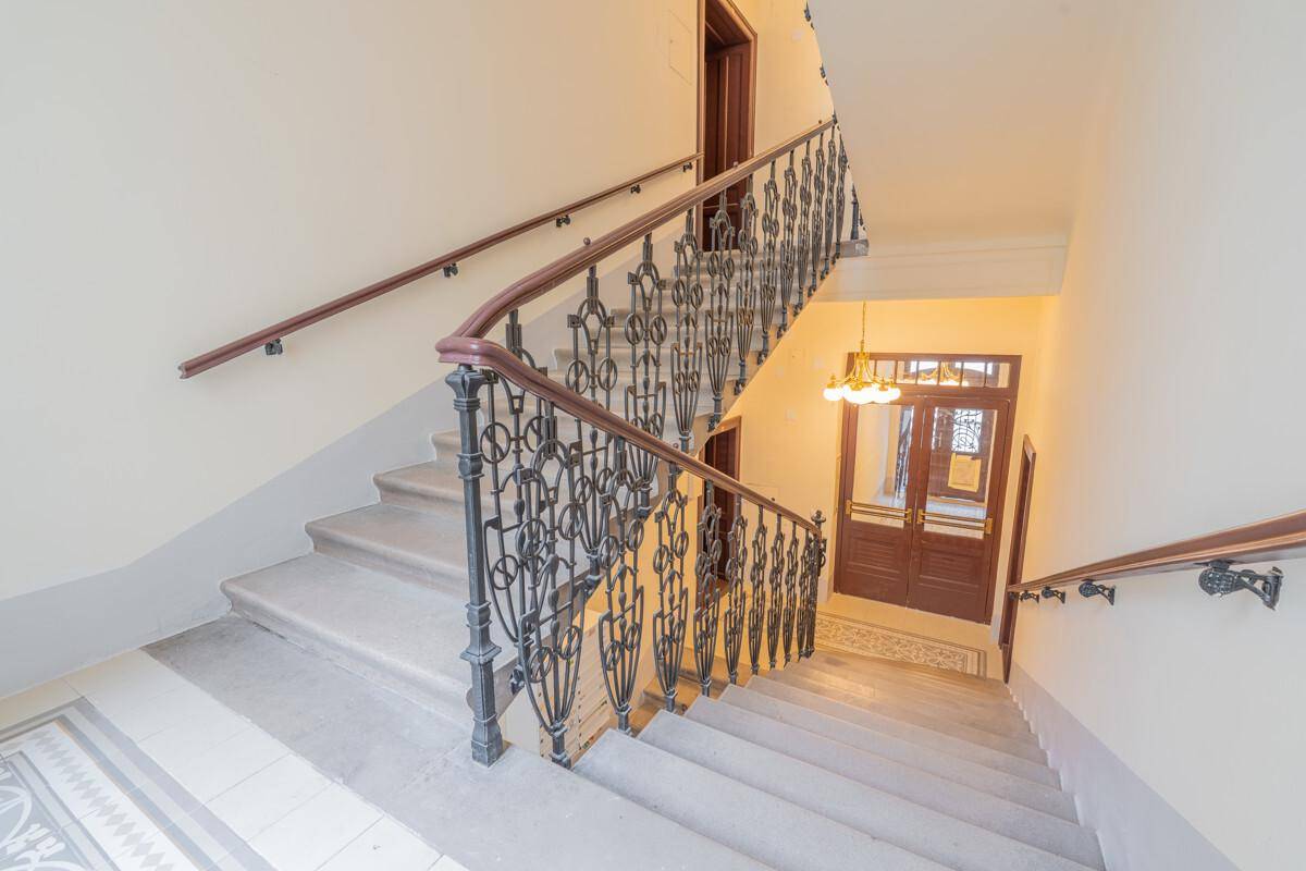 Historisches Treppenhaus mit kunstvollem schmiedeeisernem Geländer und hohen Decken.