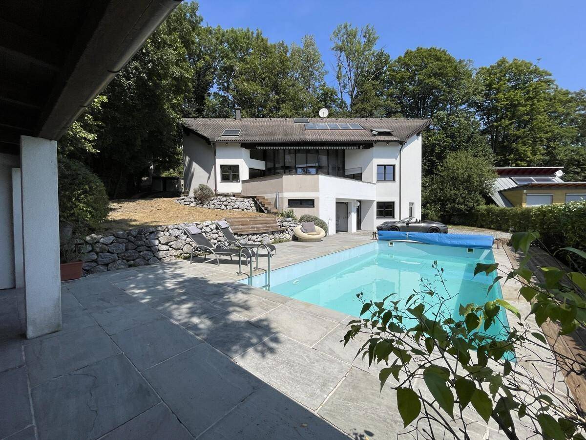 Ansicht des Hauses vom Poolbereich mit Liegestühlen und umgebender Natur.