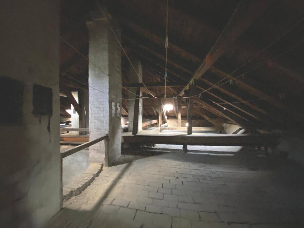 Dunkler Dachboden mit sichtbaren Holzbalken und Ziegelboden, ideal als Stauraum.