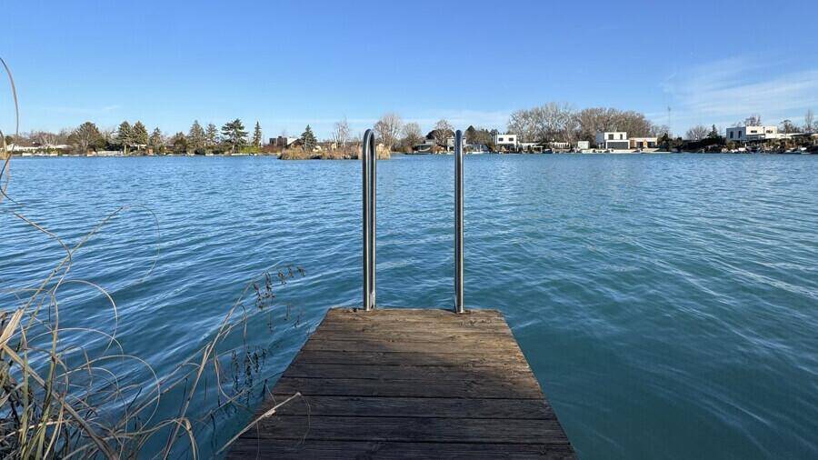 Holzsteg mit Badeleiter führt direkt ins klare Wasser des Sees unter blauem Himmel.