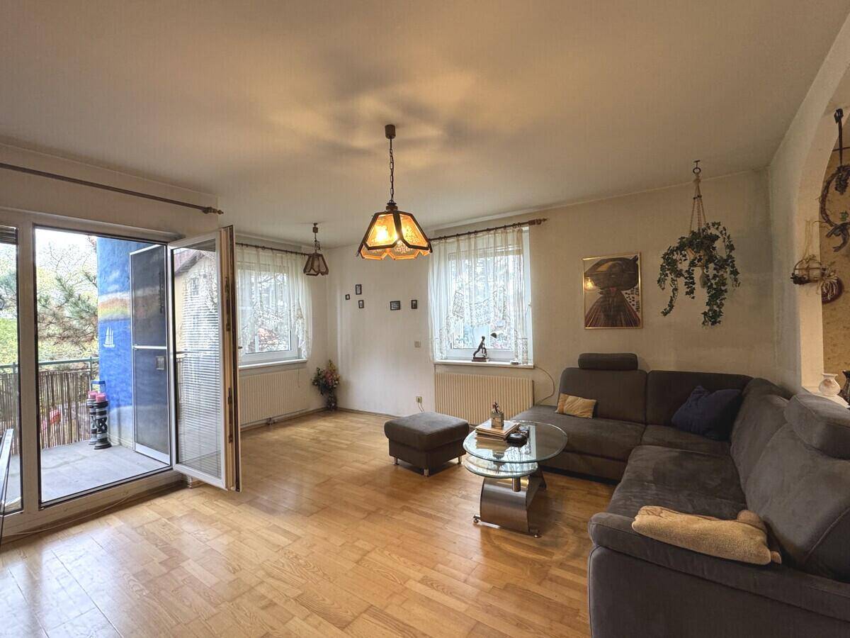 Wohnzimmer mit Parkettboden, gemütlicher Couch und Zugang zu einem Balkon.