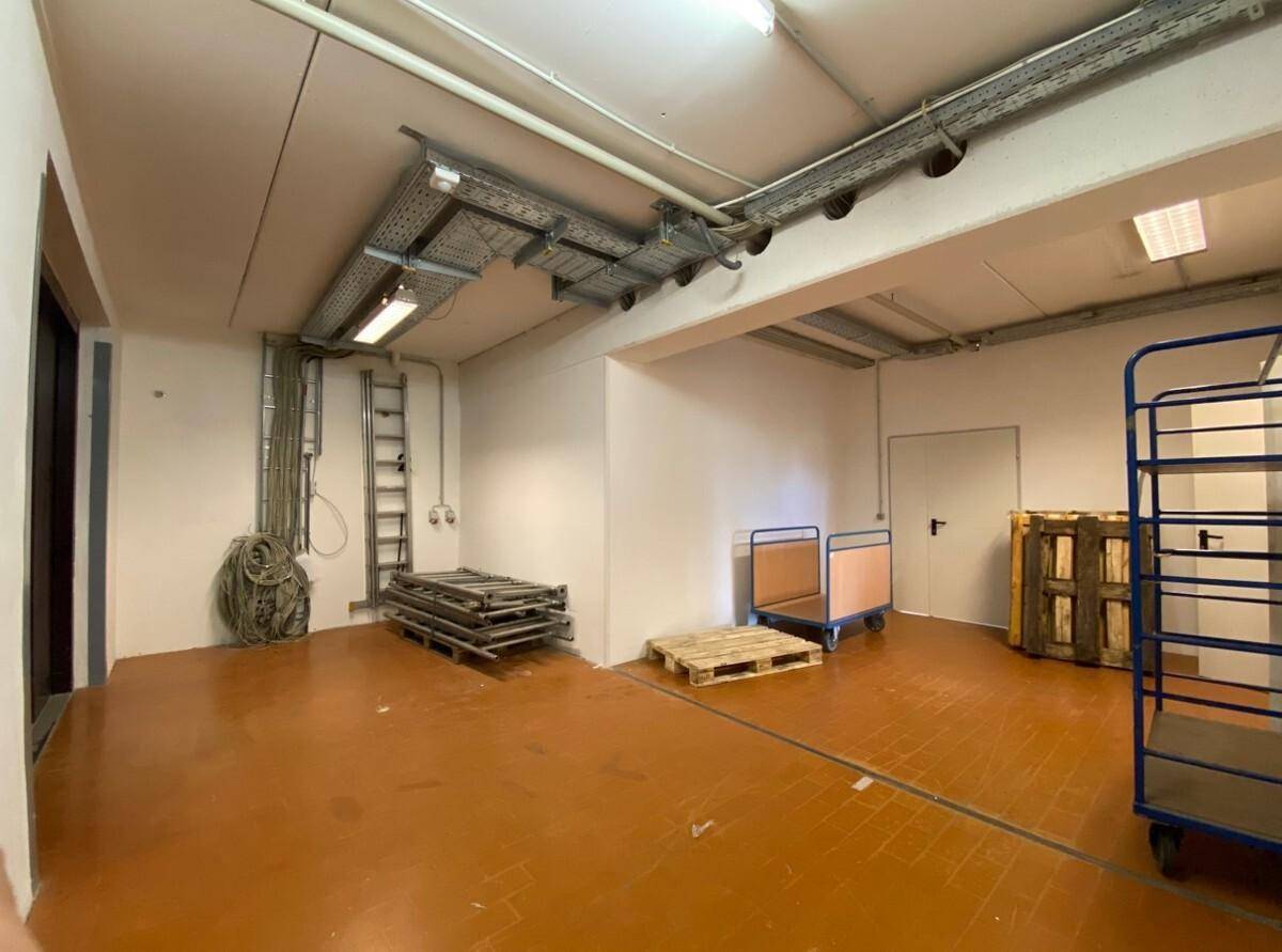 Lagerraum mit sichtbaren Kabeltrassen, Rohren an der Decke und robustem Fliesenboden.