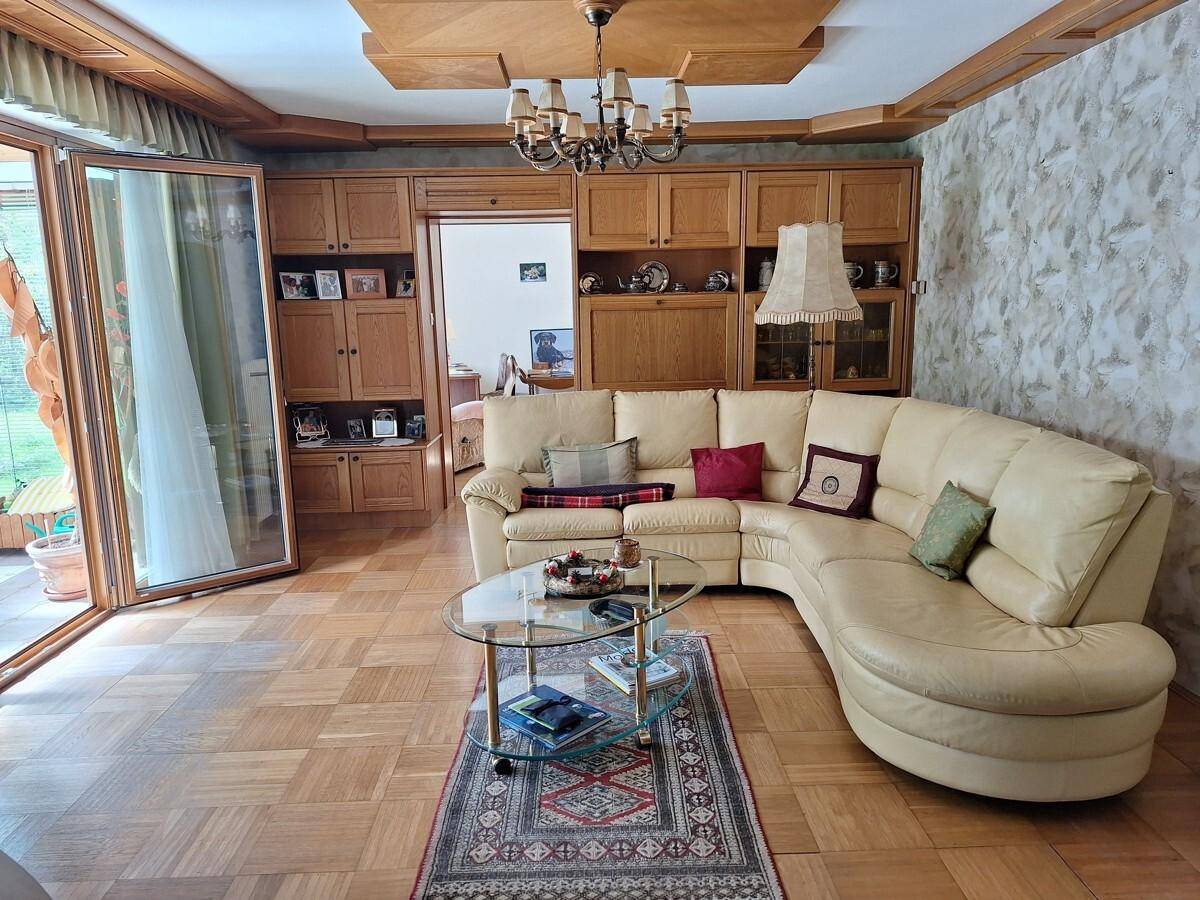 Geräumiges Wohnzimmer mit beigem Ecksofa, Holzeinbauten und Zugang zum Wintergarten, sehr wohnlich gestaltet.