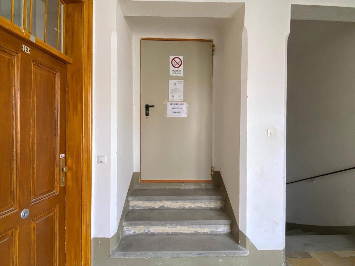 Eingangsbereich mit einer Tür, Stufen und einem gefliesten Boden in einem Altbau.