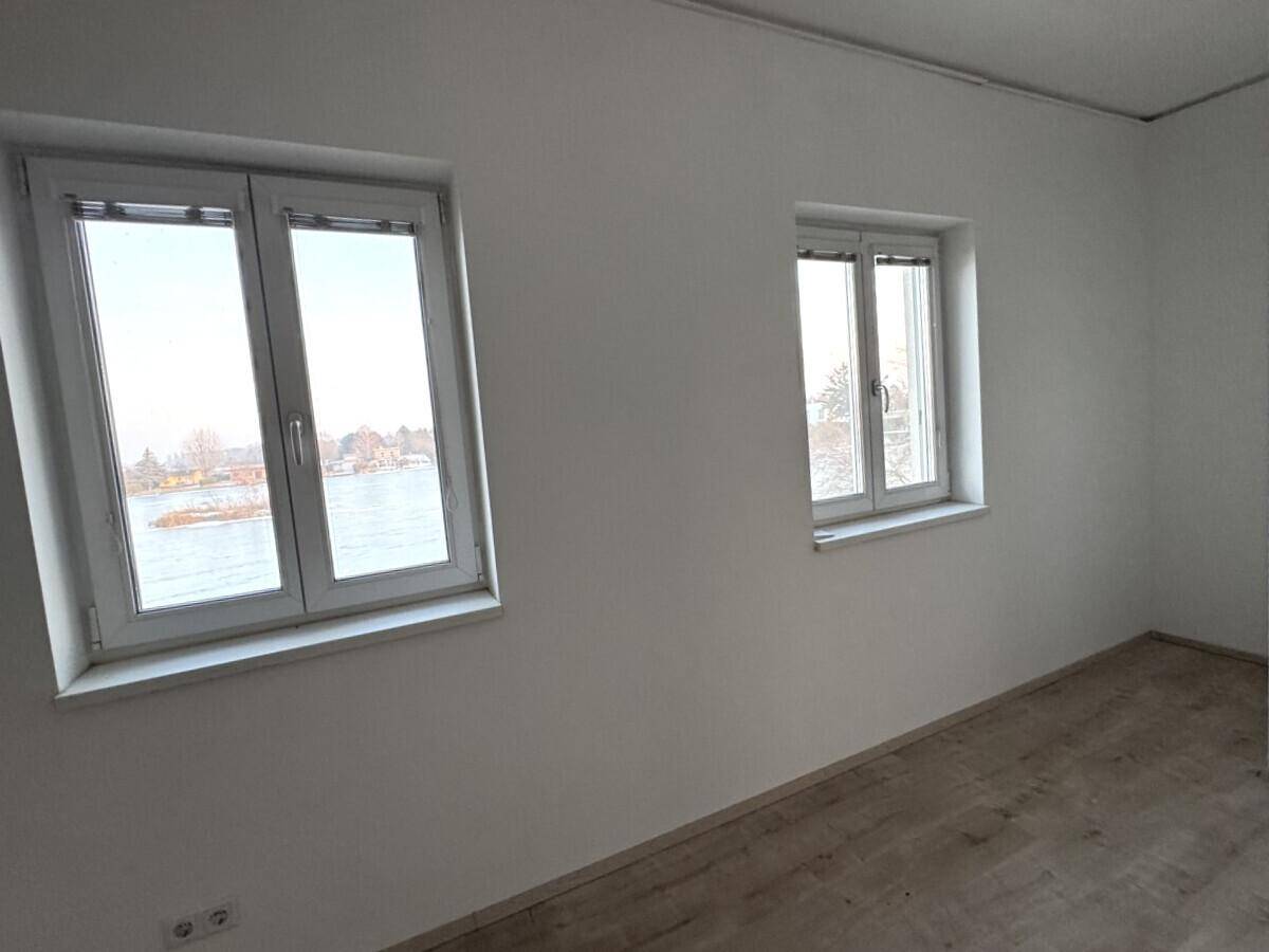 Heller Raum mit zwei Fenstern, die einen weiten Blick auf den See bieten und Holzboden.