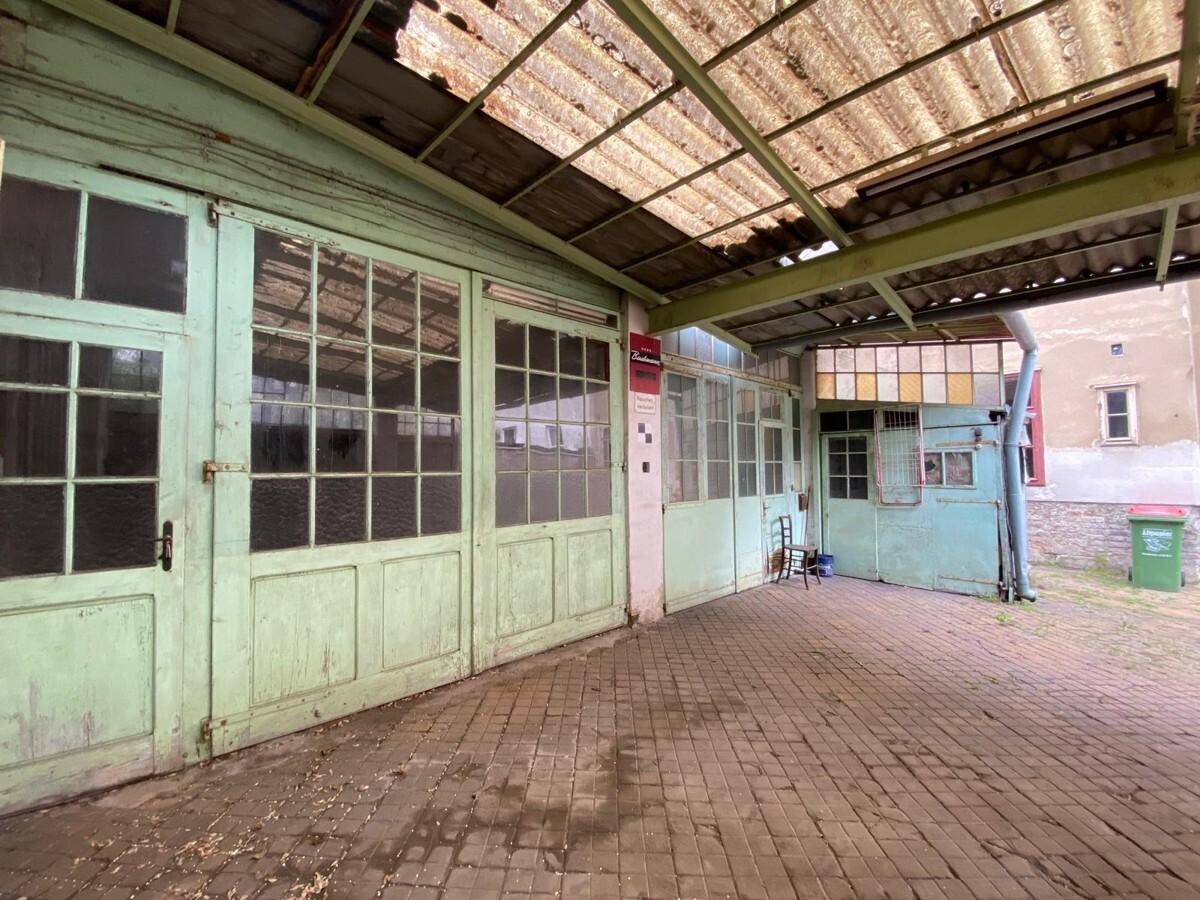 Überdachter Bereich mit alten grünen Holztoren und Wellblechdach, ideal als Garage oder Werkstatt.
