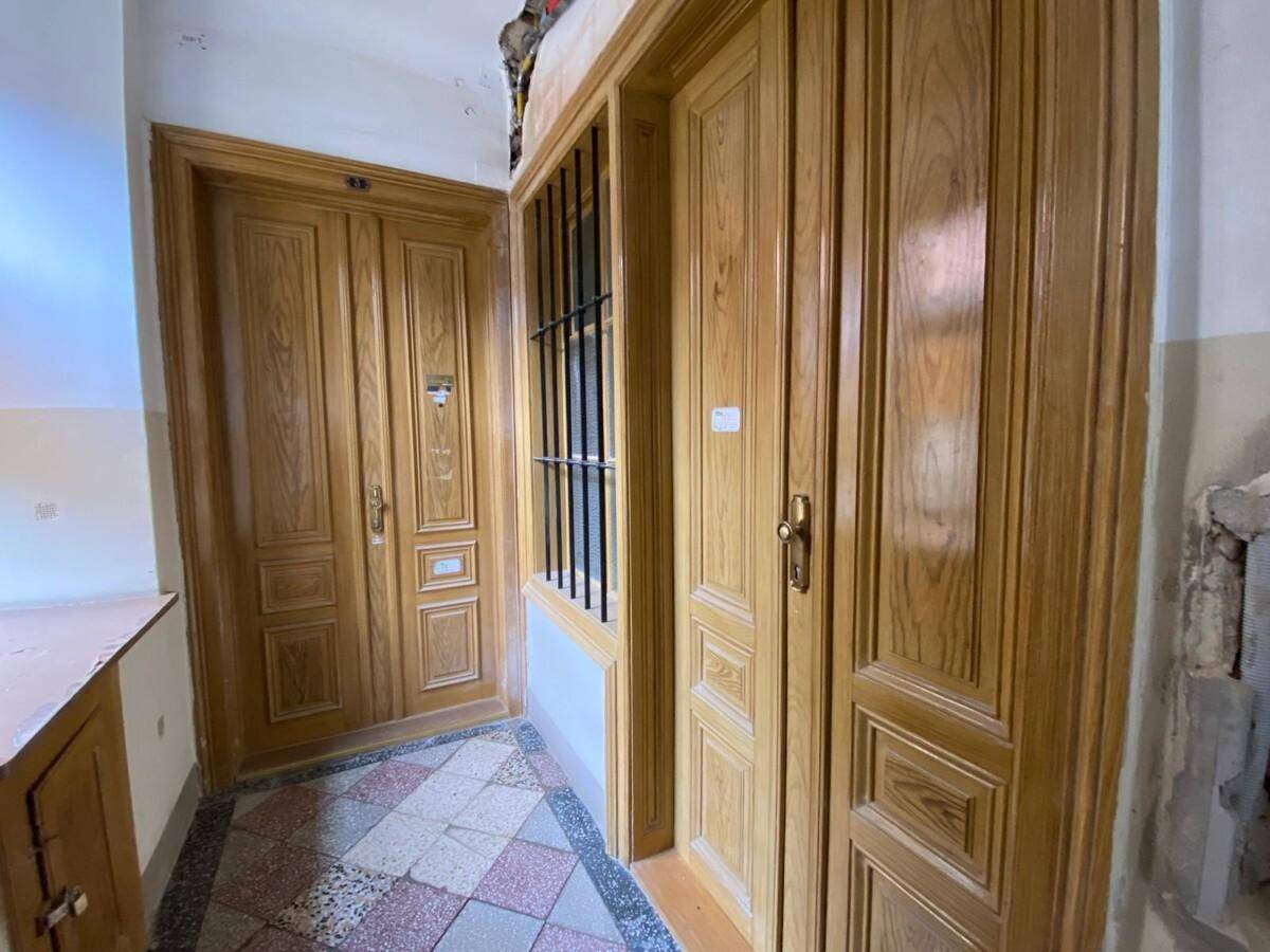 Eingangsbereich mit mehreren Holztüren, gemustertem Fliesenboden und einem Fenster mit Gitter in einem Altbau.