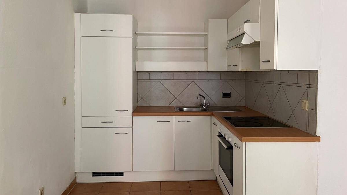 Kleine, funktionale Küche mit weißen Schränken, Holz-Arbeitsplatte und Fliesen-Rückwand.