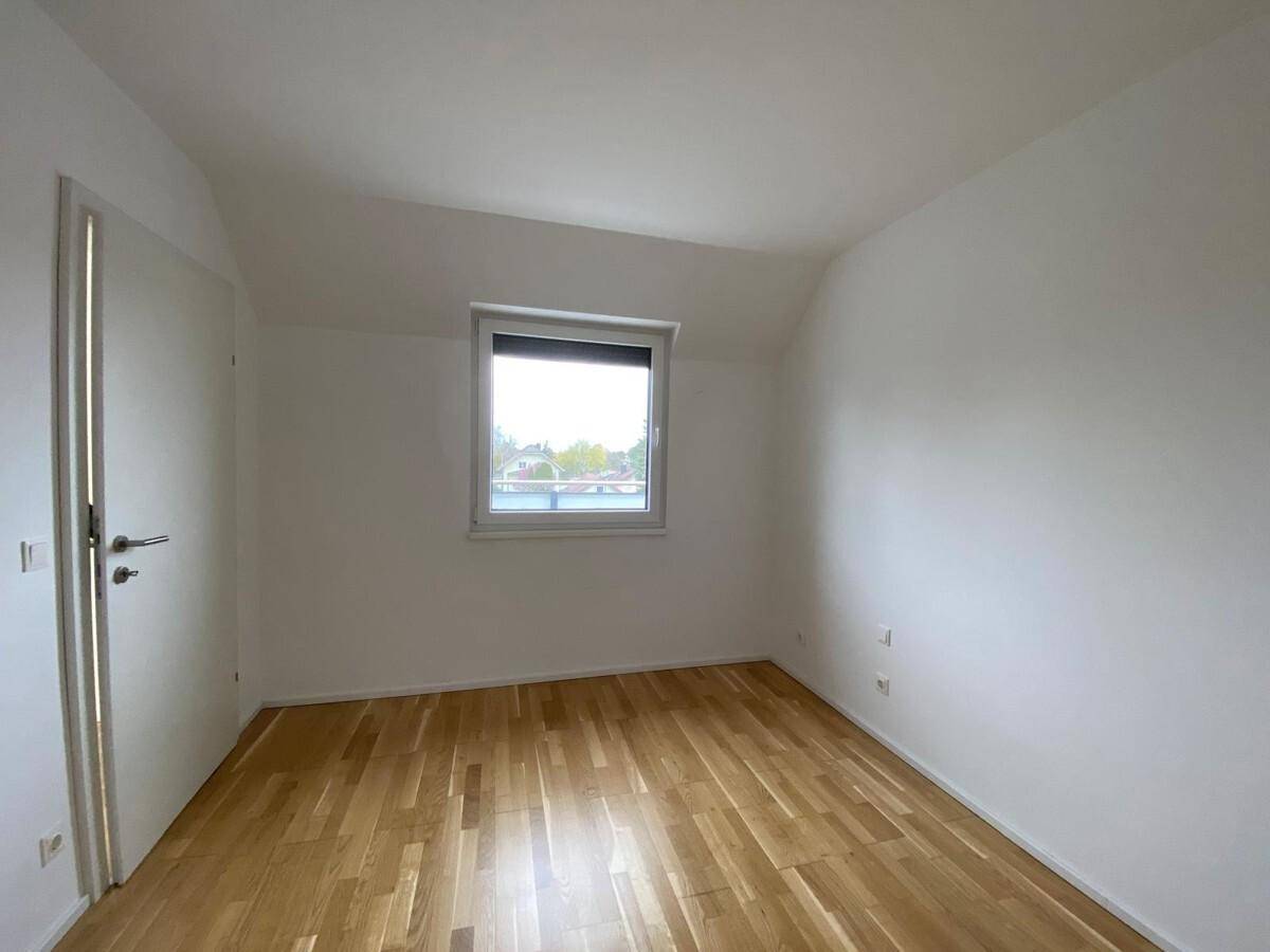 Helles, leeres Zimmer mit Holzboden und einem Fenster, ideal als Schlaf- oder Arbeitszimmer.