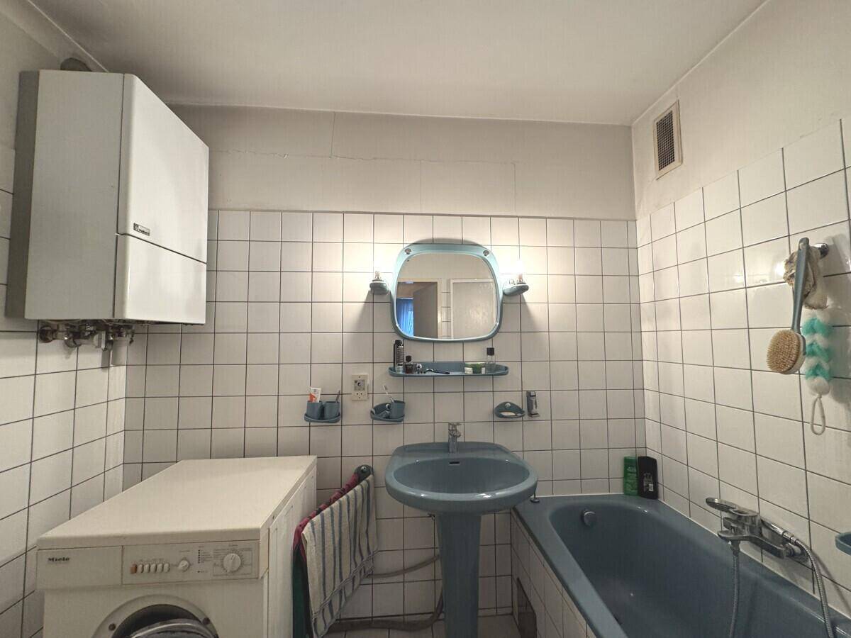 Badezimmer mit blauen Sanitärobjekten, weißen Fliesen, Badewanne und Waschmaschine.