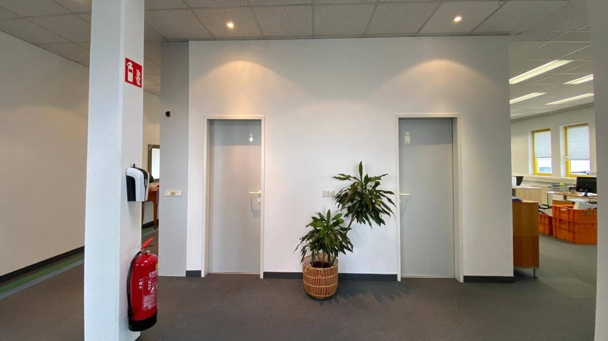 Heller Flur mit Zugang zu Toiletten, ausgestattet mit Feuerlöscher und Desinfektionsspender.