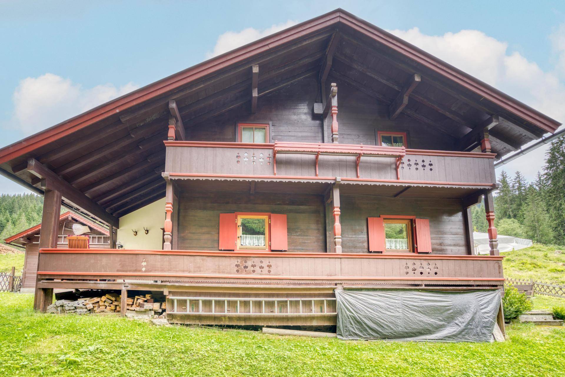 Detailansicht der Holzfassade des Chalets mit traditionellen Balkonen und roten Fensterläden.