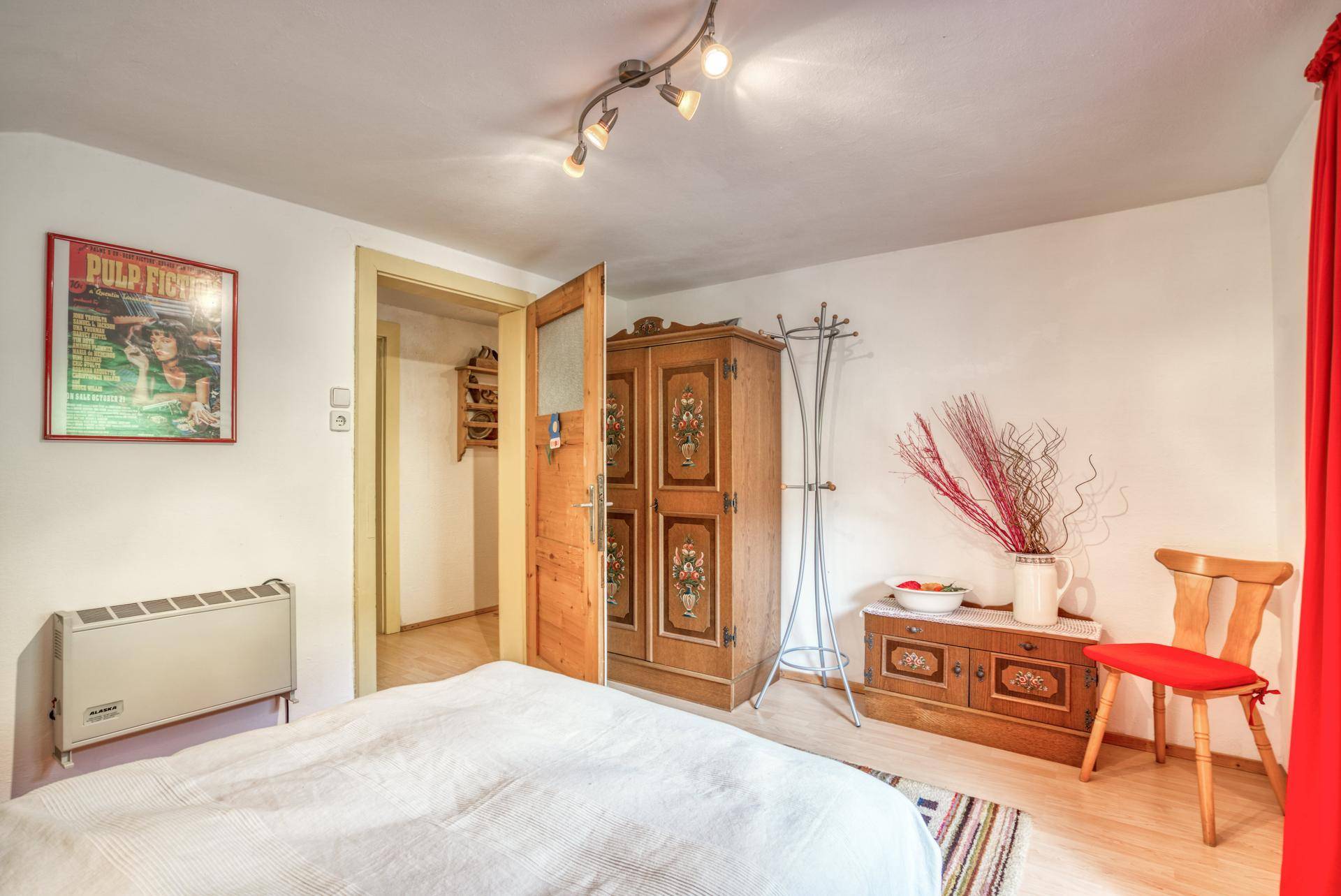 Schlafzimmer mit traditionellem bemalten Holzschrank, Doppelbett und einem Heizkörper an der Wand.
