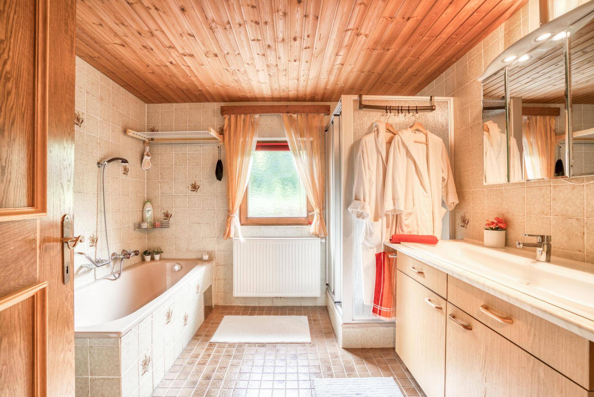 Traditionelles Badezimmer mit Badewanne, separater Dusche, Holzdecke und einem Fenster für Tageslicht.