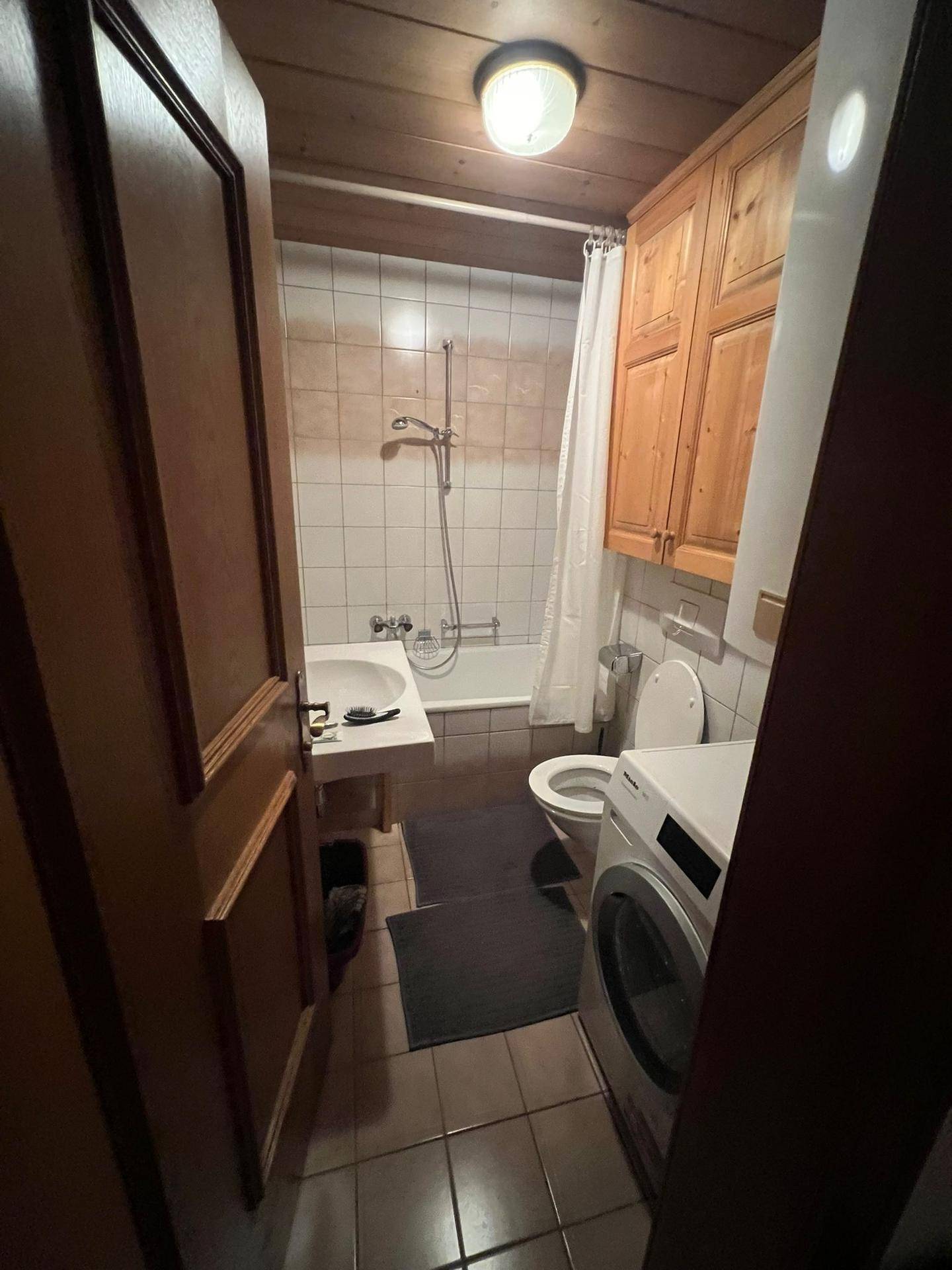 Funktionales Badezimmer mit Badewanne, Waschmaschine und traditionellen Fliesen, ausgestattet mit Holzschränken.