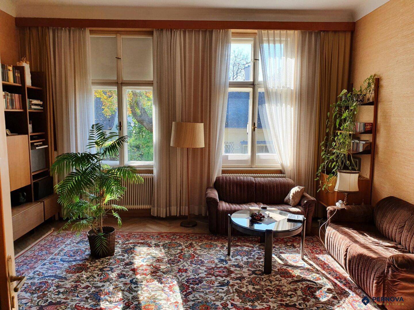 Gemütliches Wohnzimmer mit traditionellem Teppich, bequemen Sofas und großen Fenstern.