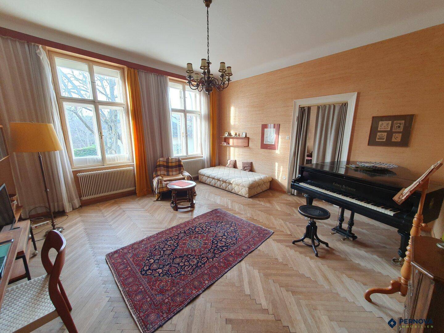 Geräumiges Wohnzimmer mit Fischgrätparkett, einem Flügel und großen Fenstern.