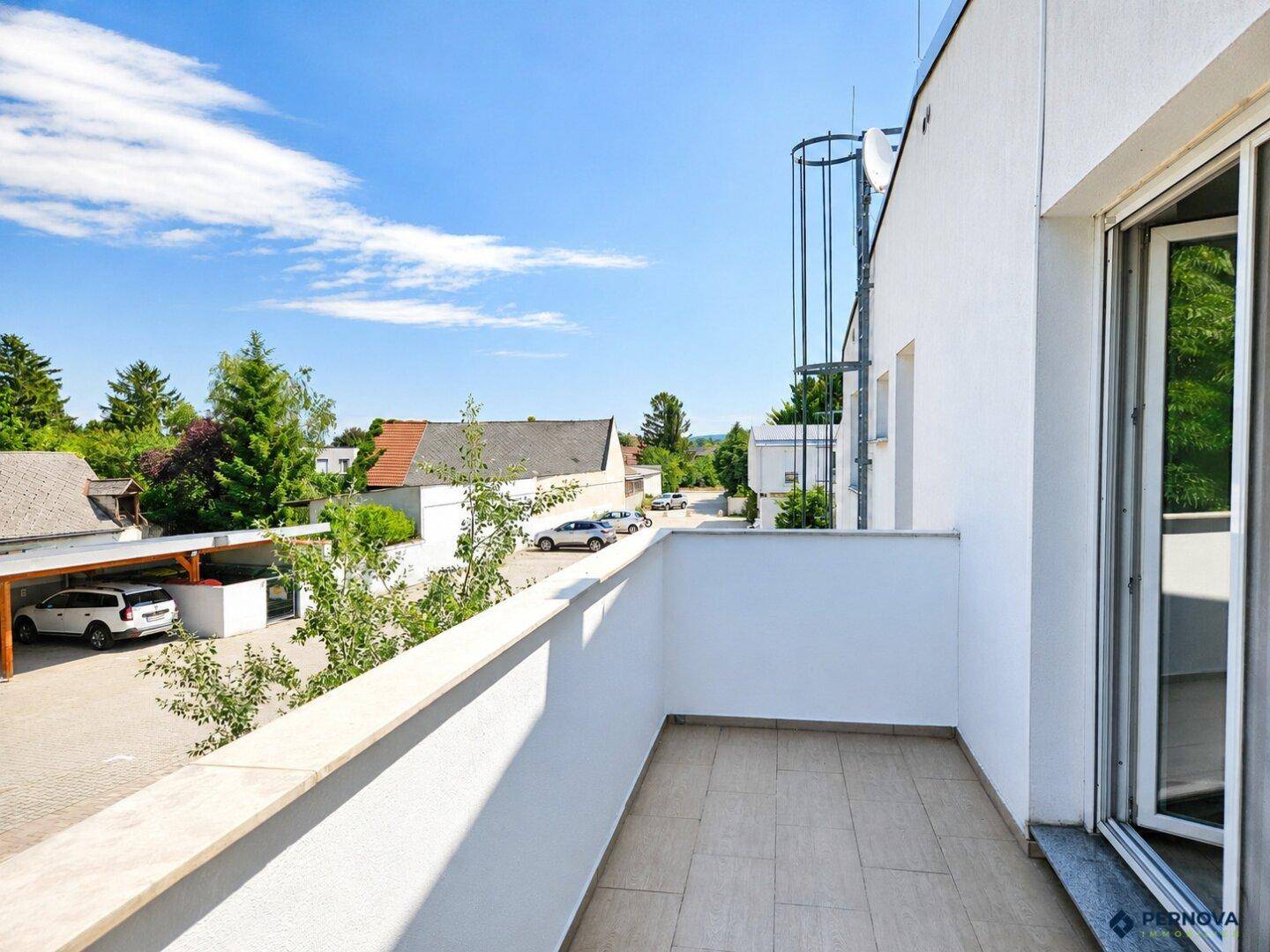 Heller Balkon mit Fliesenboden und Blick auf die Umgebung und Parkplätze.