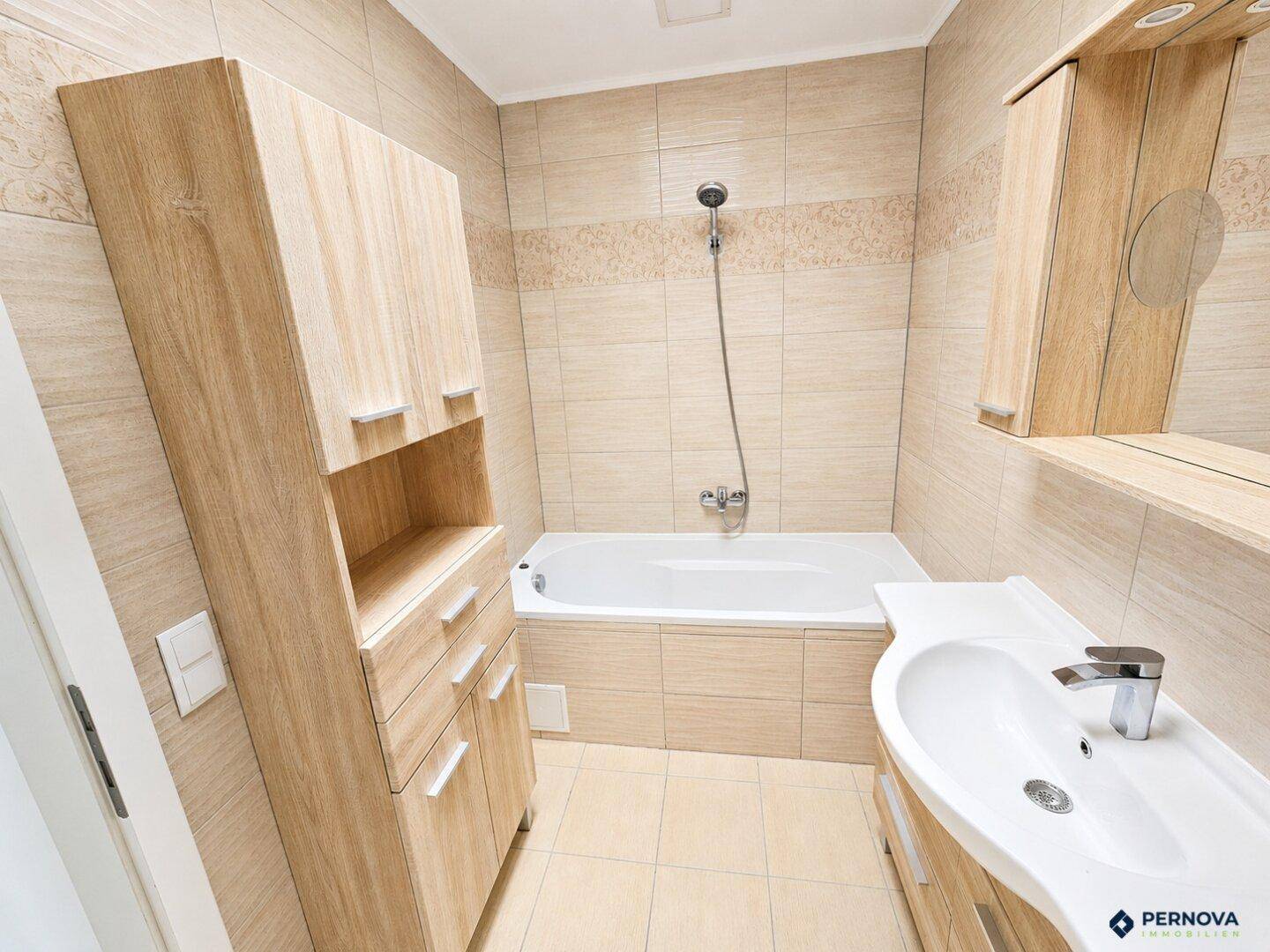 Modernes Badezimmer mit beigen Fliesen, Badewanne, Einzelwaschbecken und Holzschränken.
