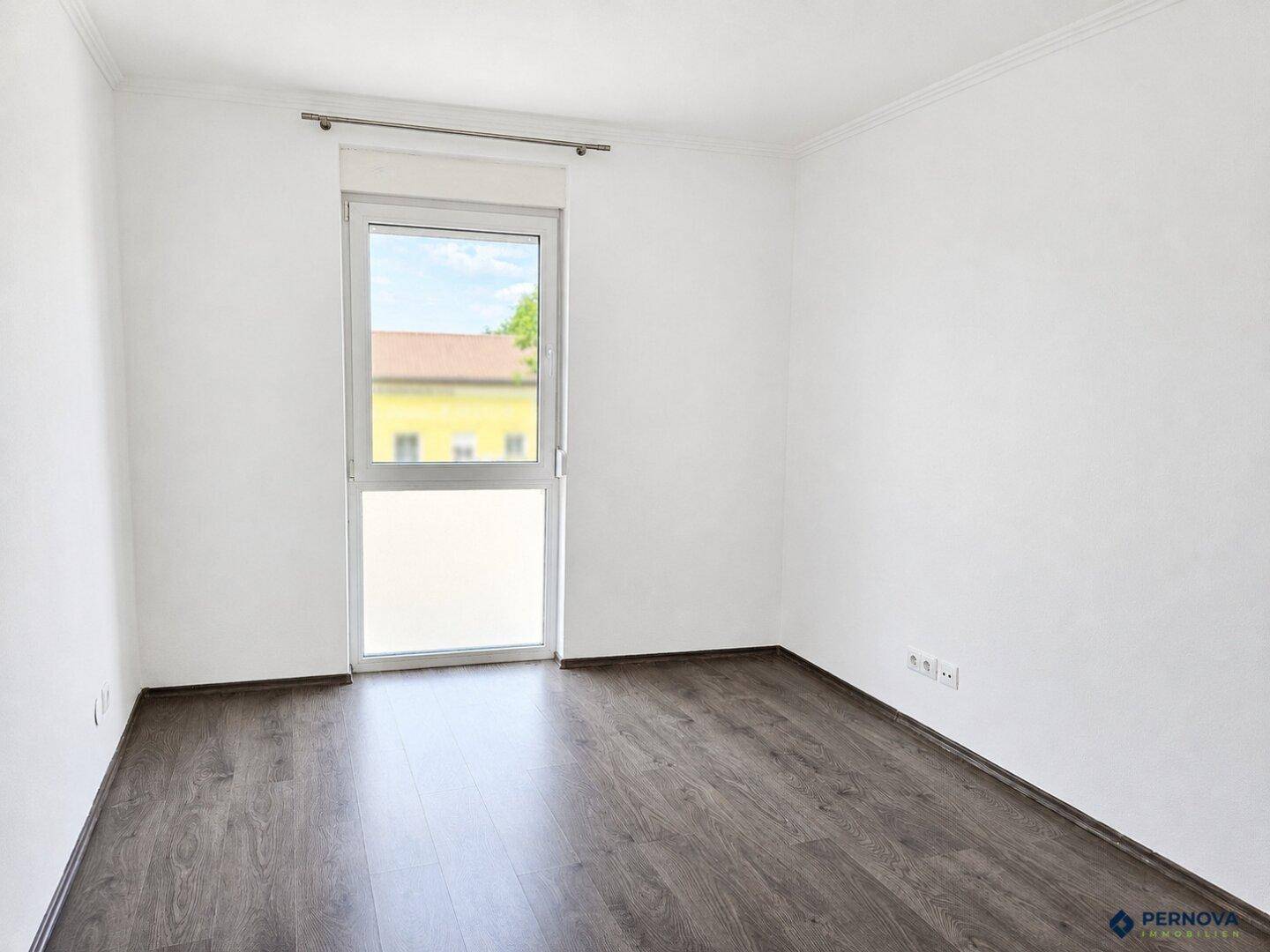 Helles Schlafzimmer mit Laminatboden und einem großen Fenster mit Blick nach draußen.