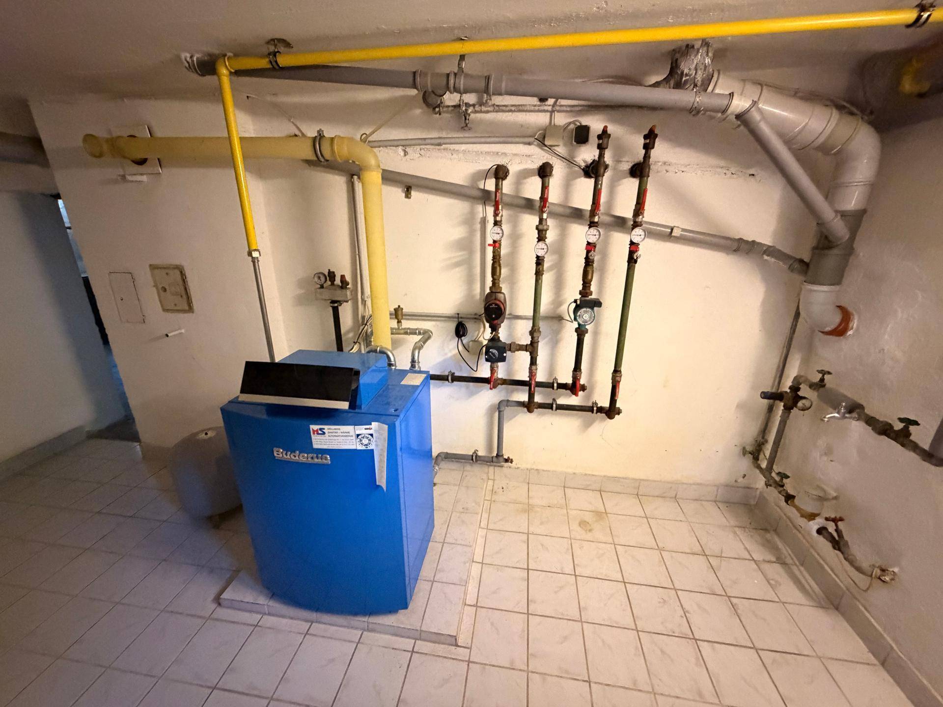Heizungsraum im Keller mit einem Buderus-Heizkessel und sichtbaren Rohrleitungen an der Wand.