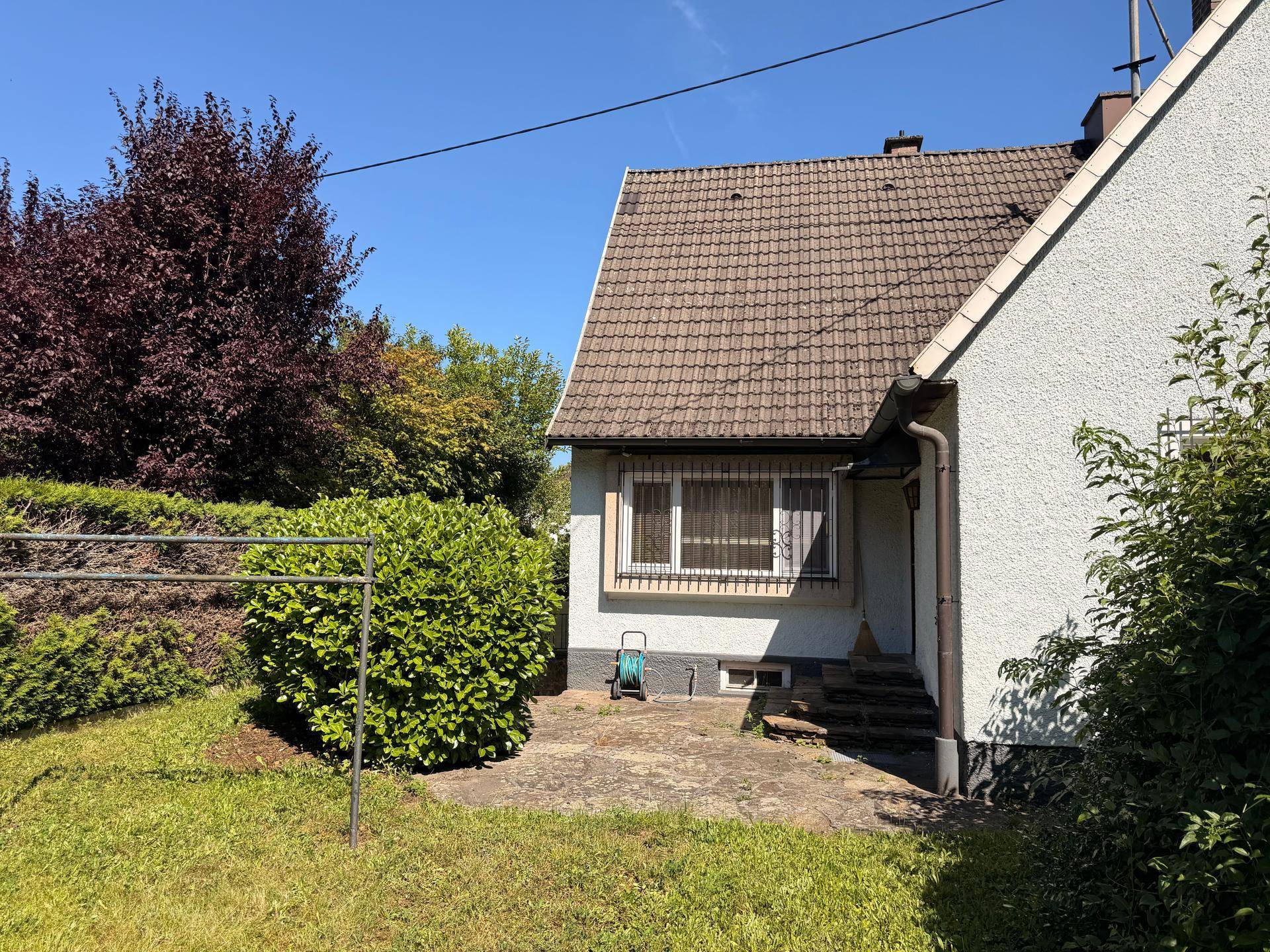 Rückseite des Hauses mit einer kleinen gepflasterten Fläche und einem Wäscheständer im Garten.