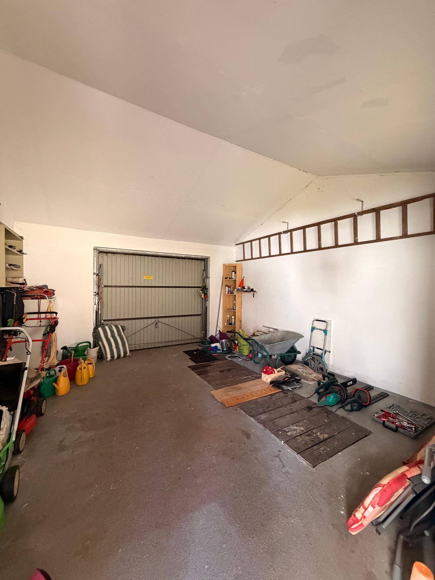Geräumige Garage mit einem Rolltor, viel Stauraum und verschiedenen Gartengeräten.