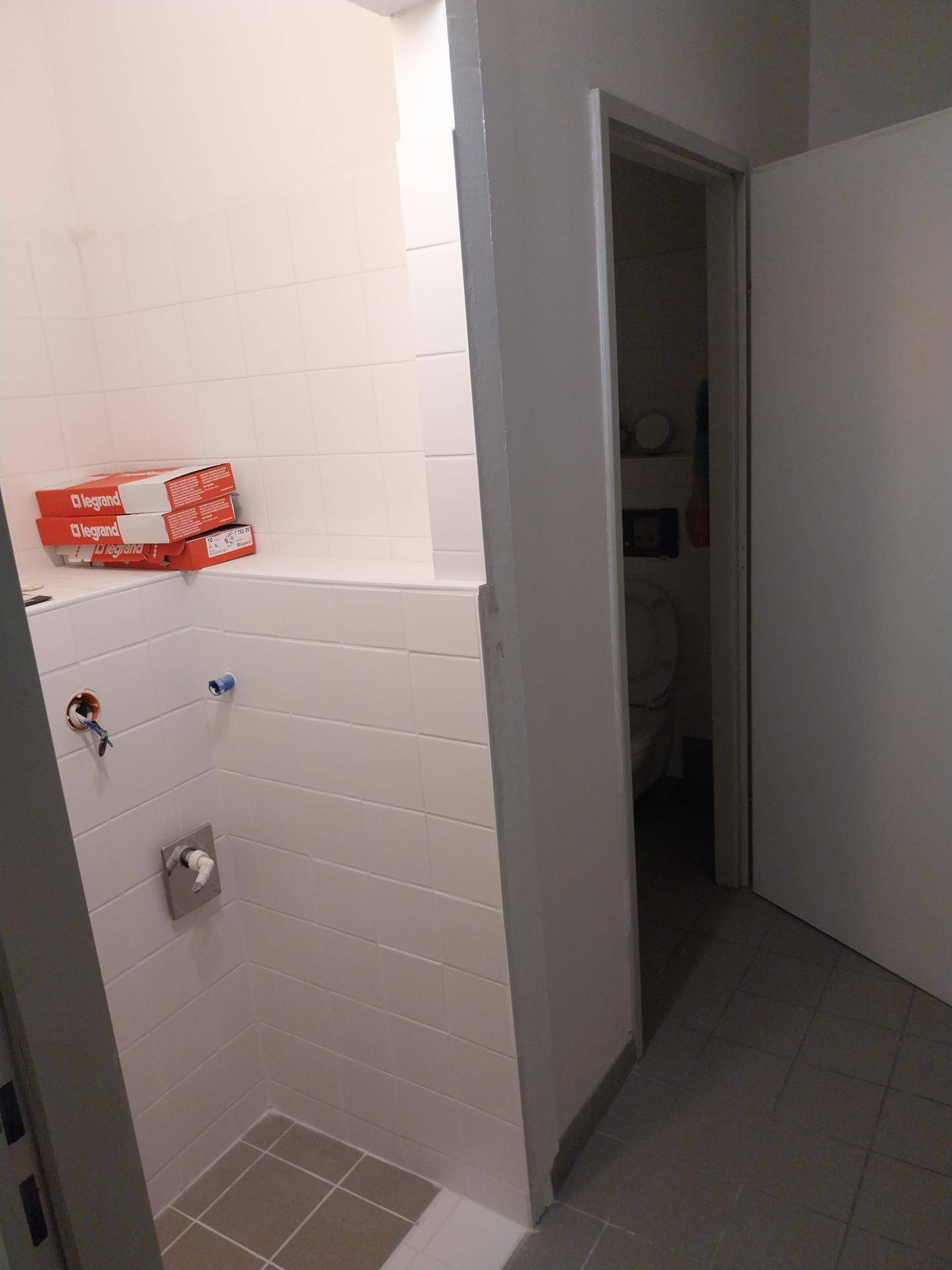 Badezimmer im Bau mit gefliester Duschfläche und vorbereiteten Anschlüssen.