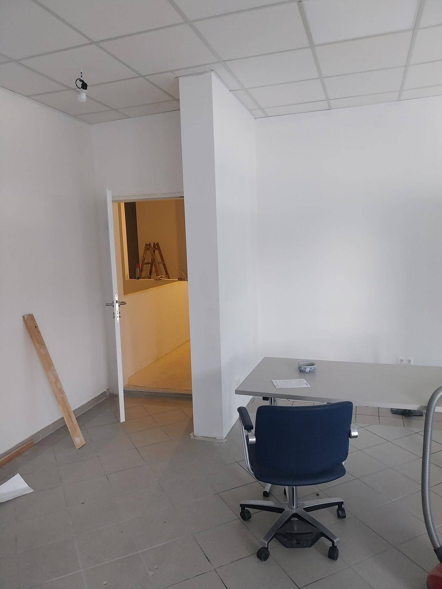 Büroraum im Bau mit einem Schreibtisch, Bürostuhl und Blick in einen weiteren Raum.