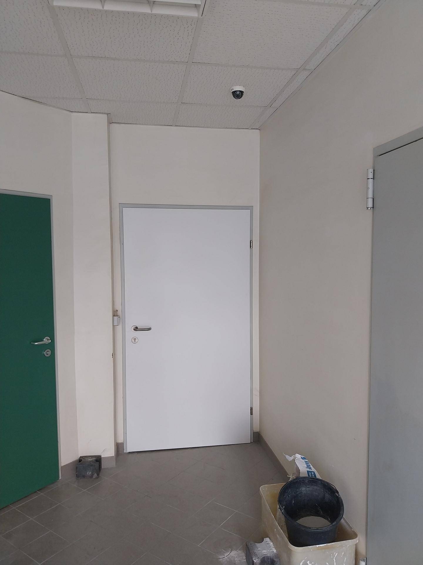 Flur mit mehreren Türen, abgehängter Decke und einer Überwachungskamera.